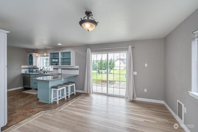 kitchen with a breakfast bar area, hanging light fixtures, stainless steel dishwasher, kitchen peninsula, and light hardwood / wood-style flooring