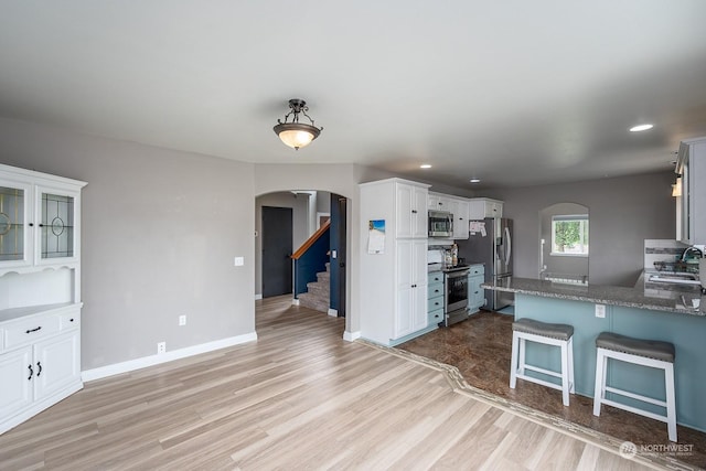 kitchen with sink, appliances with stainless steel finishes, white cabinetry, light hardwood / wood-style floors, and a kitchen bar