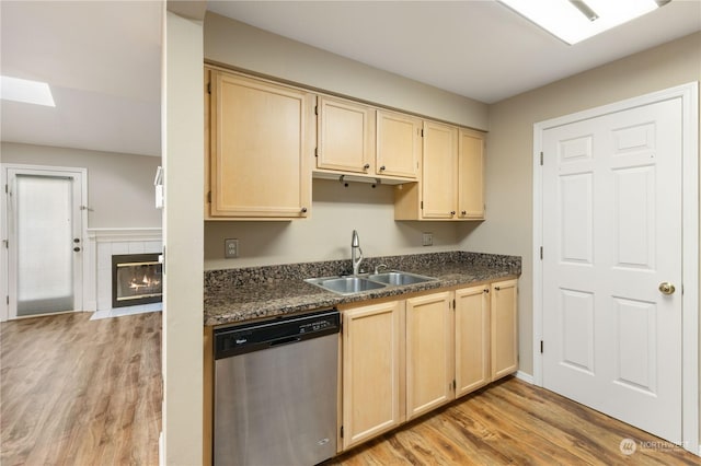 kitchen featuring a tiled fireplace, dishwasher, sink, and light wood-type flooring