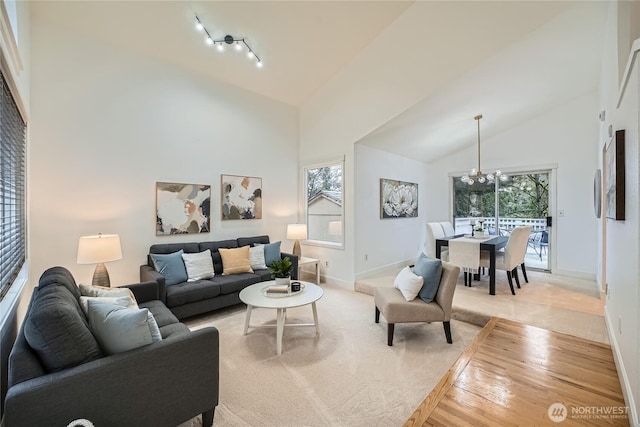 living room with a chandelier, track lighting, high vaulted ceiling, light wood-type flooring, and baseboards