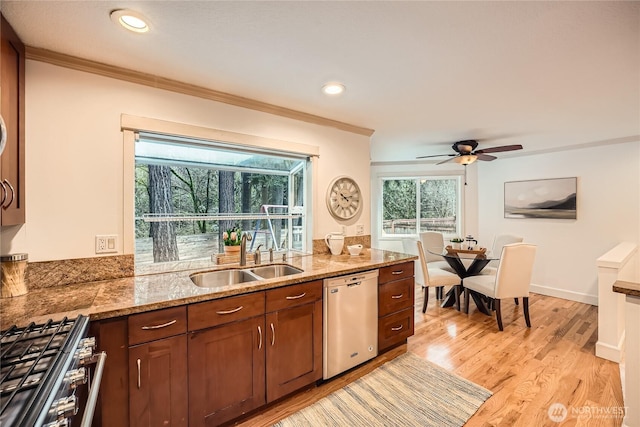 kitchen featuring crown molding, stainless steel appliances, light wood-style flooring, a sink, and light stone countertops