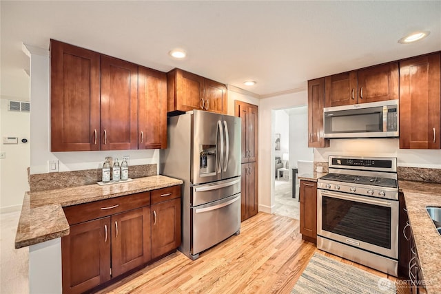 kitchen with stainless steel appliances, light wood-style flooring, visible vents, and light stone counters