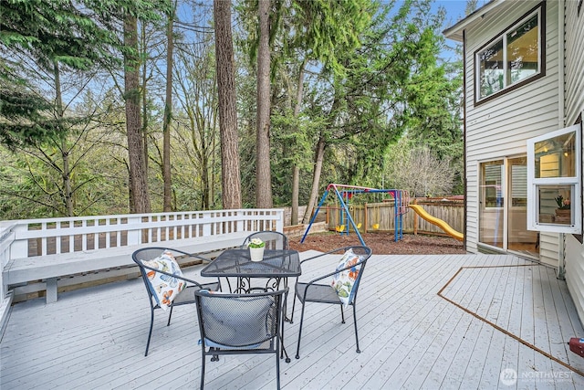 wooden deck with outdoor dining area, a playground, and fence