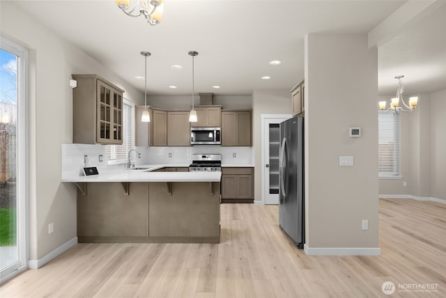 kitchen with light wood finished floors, a sink, a peninsula, a chandelier, and stainless steel appliances