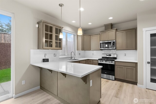 kitchen with a peninsula, appliances with stainless steel finishes, glass insert cabinets, and tasteful backsplash