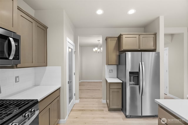 kitchen with an inviting chandelier, backsplash, light countertops, and appliances with stainless steel finishes
