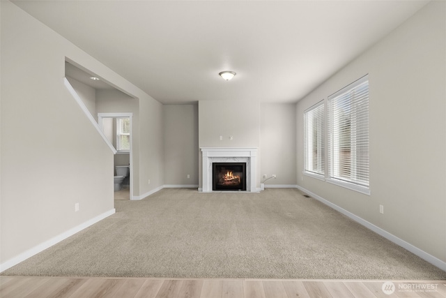 unfurnished living room with light colored carpet, light wood-type flooring, baseboards, and a premium fireplace
