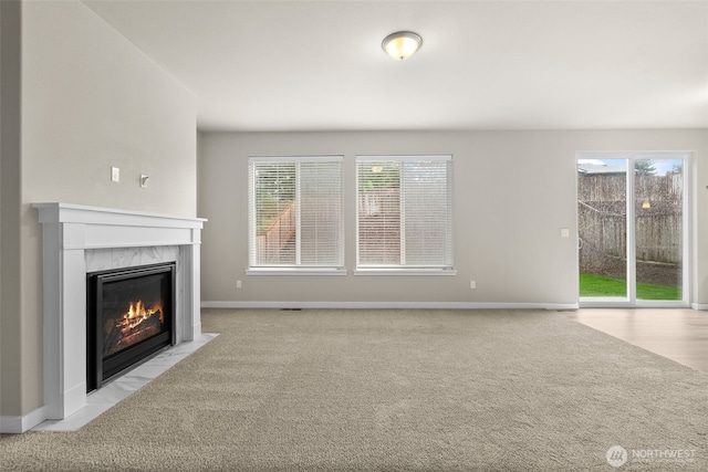 unfurnished living room with carpet, a healthy amount of sunlight, and a premium fireplace