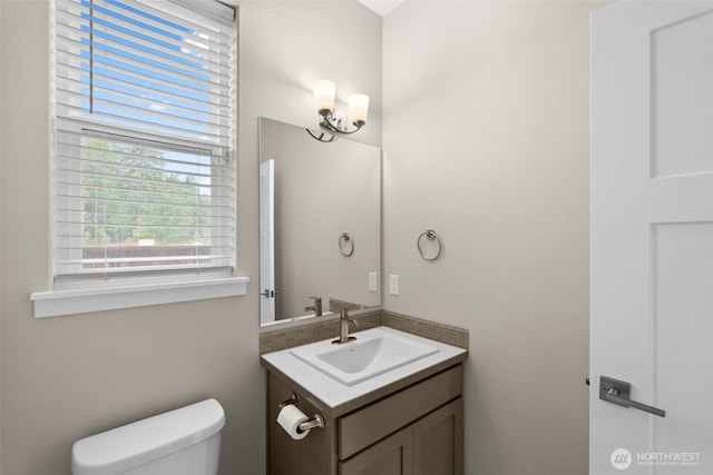 half bath with toilet, vanity, and a healthy amount of sunlight
