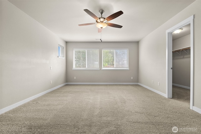 unfurnished bedroom featuring baseboards, ceiling fan, light colored carpet, and a walk in closet