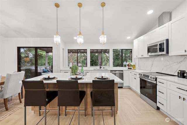 kitchen with tasteful backsplash, light parquet flooring, stainless steel appliances, and decorative light fixtures