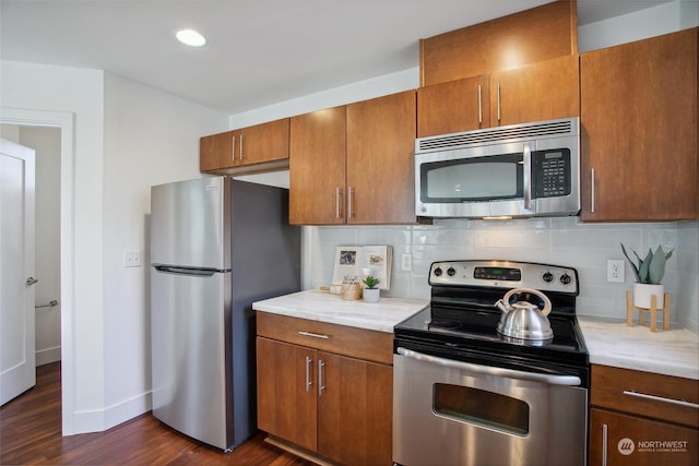 kitchen with tasteful backsplash, light stone counters, dark hardwood / wood-style floors, and appliances with stainless steel finishes