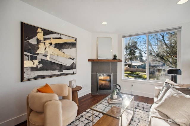 living room with a tiled fireplace and dark wood-type flooring