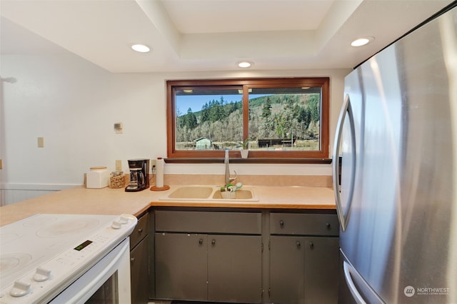 kitchen with electric range, gray cabinetry, a sink, freestanding refrigerator, and light countertops