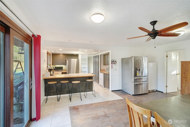 kitchen with a breakfast bar, freestanding refrigerator, stainless steel fridge, a peninsula, and light countertops