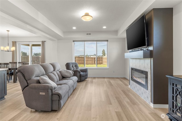 living room with a tile fireplace, a raised ceiling, a chandelier, and light hardwood / wood-style flooring