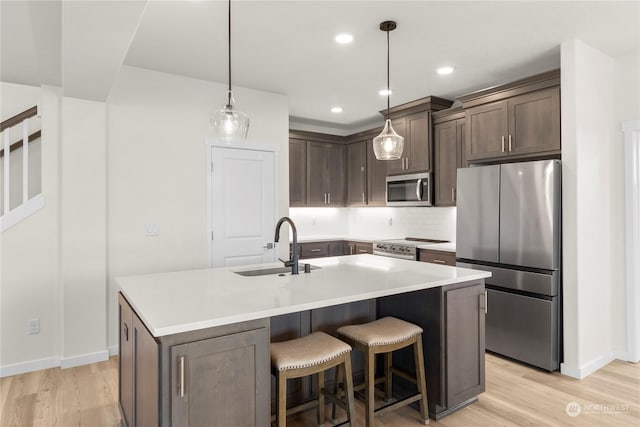 kitchen with sink, stainless steel appliances, a kitchen island with sink, and pendant lighting