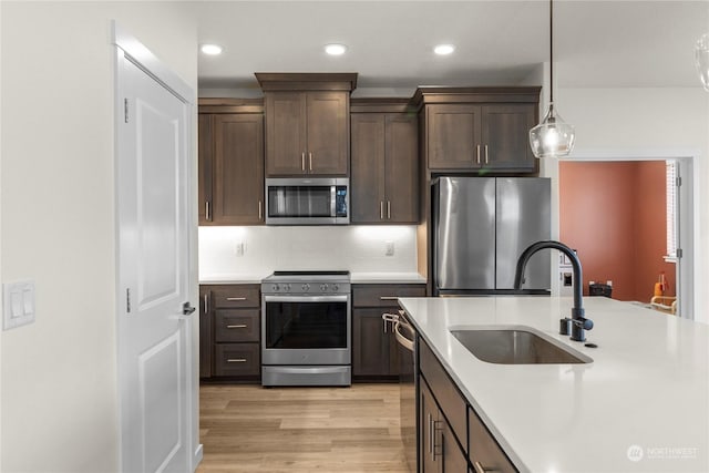 kitchen with stainless steel appliances, dark brown cabinetry, sink, backsplash, and pendant lighting