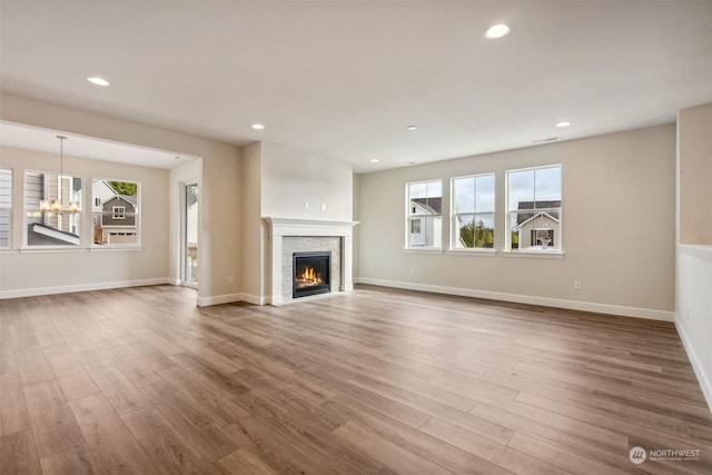 unfurnished living room with a healthy amount of sunlight, a stone fireplace, light hardwood / wood-style floors, and a notable chandelier