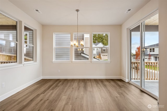 unfurnished dining area featuring a notable chandelier, wood-type flooring, and a healthy amount of sunlight