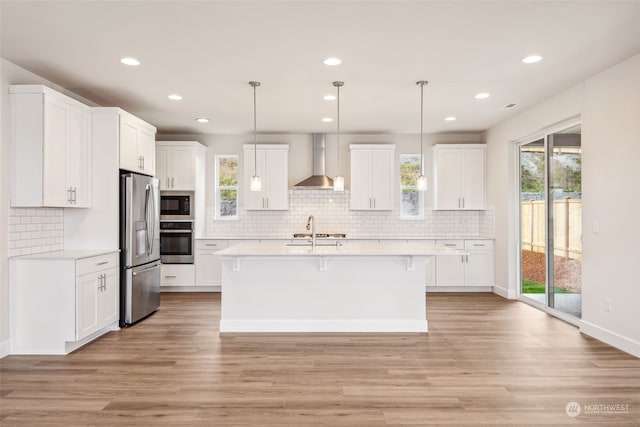 kitchen with white cabinetry, wall chimney range hood, decorative light fixtures, and appliances with stainless steel finishes