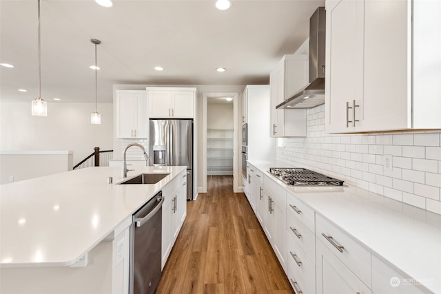 kitchen with hanging light fixtures, appliances with stainless steel finishes, white cabinets, wall chimney range hood, and backsplash