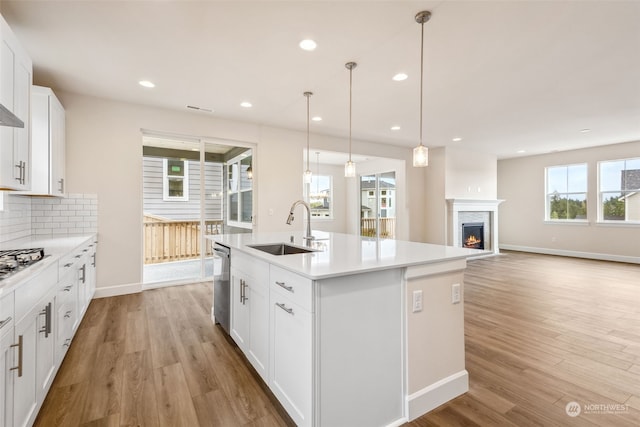 kitchen featuring sink, white cabinetry, decorative light fixtures, appliances with stainless steel finishes, and an island with sink