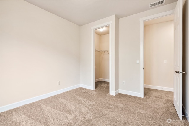 unfurnished bedroom with a walk in closet, light colored carpet, and a closet