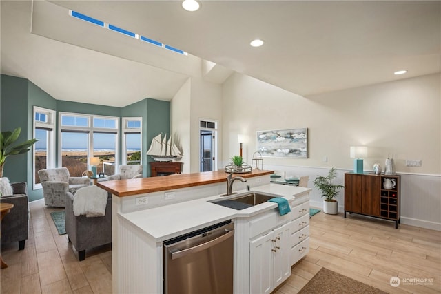 kitchen with sink, butcher block countertops, white cabinetry, dishwasher, and a kitchen island with sink