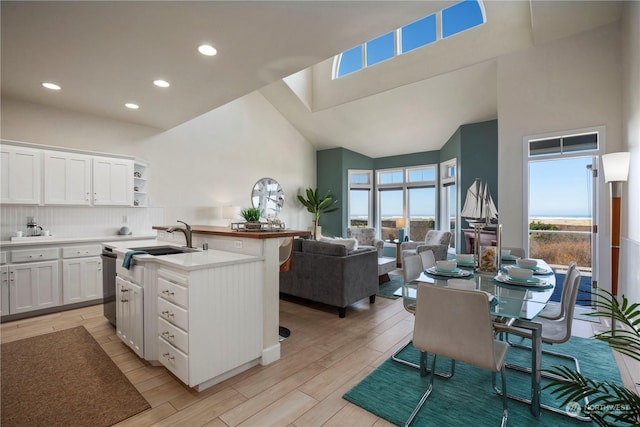 kitchen featuring sink, white cabinets, a center island with sink, decorative backsplash, and light wood-type flooring