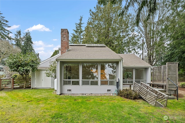 rear view of property with roof with shingles, a chimney, a lawn, a sunroom, and roof mounted solar panels