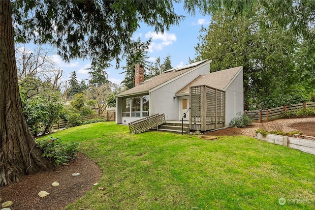 rear view of house with a lawn, a chimney, a fenced backyard, and a sunroom