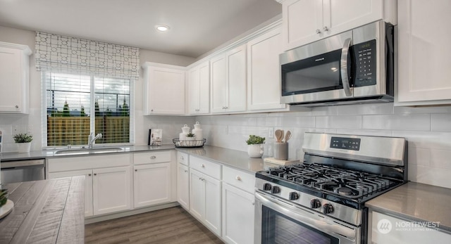 kitchen with appliances with stainless steel finishes, sink, hardwood / wood-style floors, and white cabinets