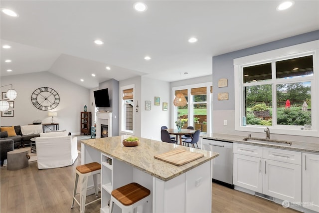 kitchen featuring a kitchen island, white cabinetry, sink, stainless steel dishwasher, and light stone countertops