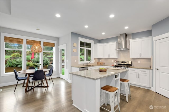 kitchen featuring hanging light fixtures, sink, wall chimney range hood, and white cabinets