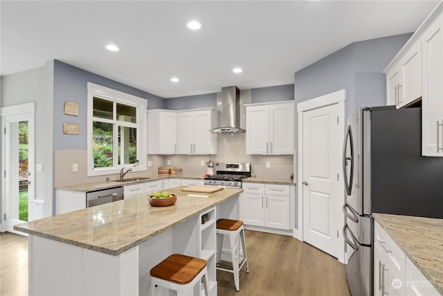 kitchen featuring appliances with stainless steel finishes, a center island, a breakfast bar area, and wall chimney exhaust hood