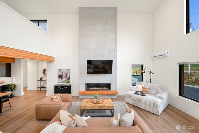 living room with a towering ceiling, a fireplace, a wall unit AC, and wood-type flooring