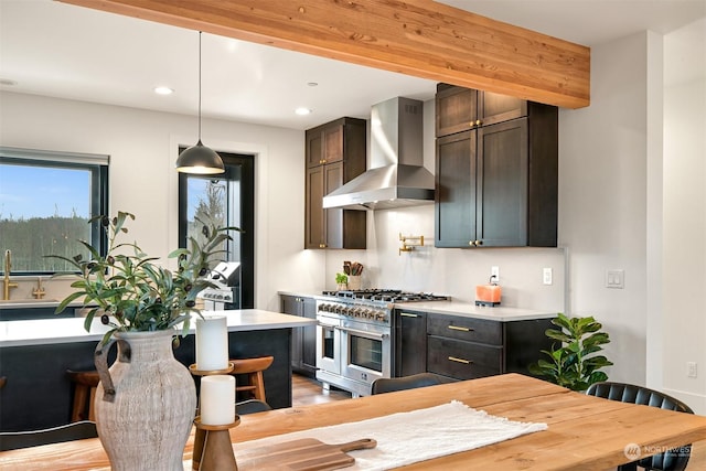 kitchen featuring dark brown cabinetry, wall chimney exhaust hood, a center island, hanging light fixtures, and range with two ovens