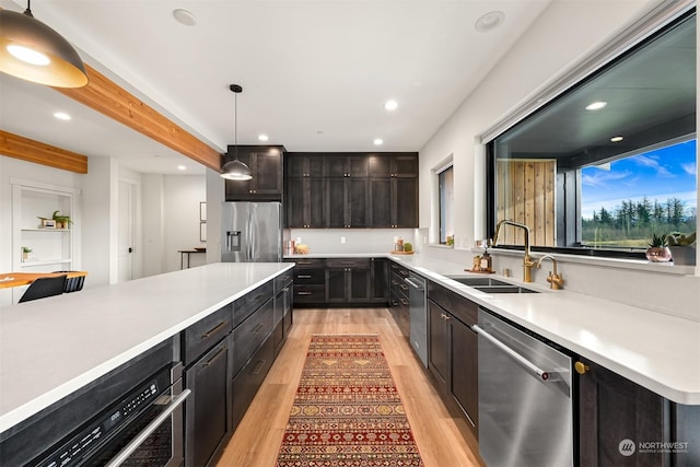 kitchen featuring pendant lighting, beamed ceiling, sink, light hardwood / wood-style floors, and stainless steel appliances