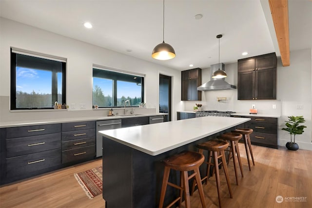 kitchen with sink, a breakfast bar, appliances with stainless steel finishes, a kitchen island, and wall chimney exhaust hood