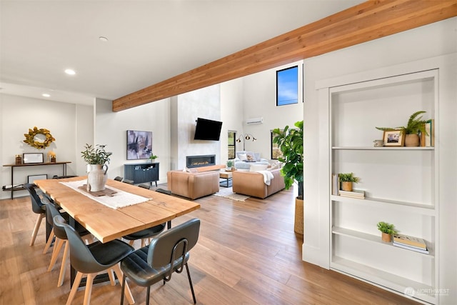 dining space with beamed ceiling, wood-type flooring, and a large fireplace