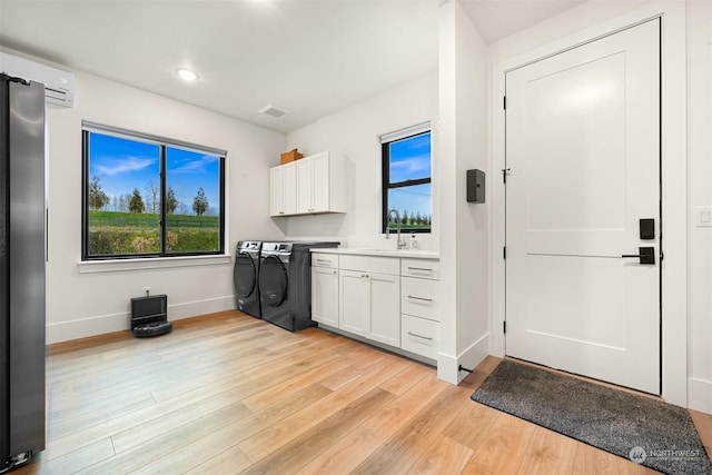 laundry room with sink, plenty of natural light, cabinets, a wall mounted air conditioner, and light wood-type flooring