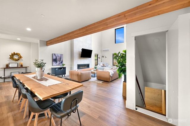 dining space with beam ceiling, light hardwood / wood-style floors, and a large fireplace