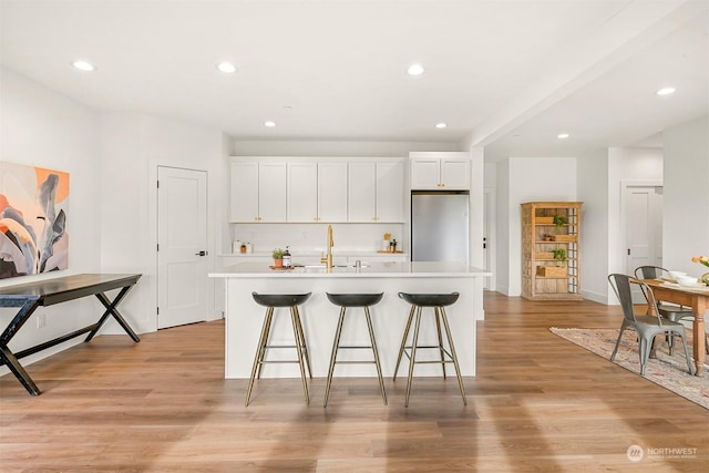 kitchen featuring white cabinetry, a center island with sink, stainless steel refrigerator, and light hardwood / wood-style floors