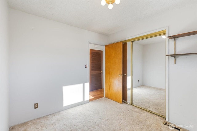 unfurnished bedroom with light carpet, a closet, and a textured ceiling