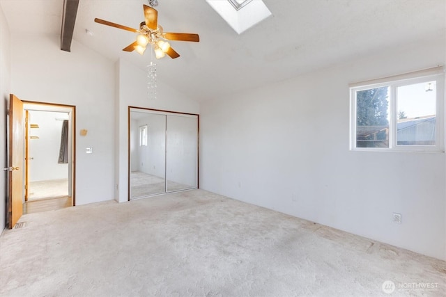 unfurnished bedroom with a closet, beamed ceiling, a skylight, carpet, and ceiling fan