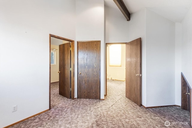 unfurnished bedroom featuring a high ceiling, a closet, light colored carpet, and beam ceiling