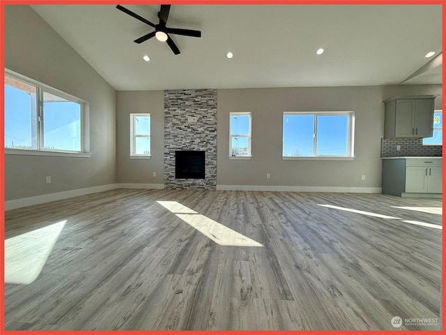 unfurnished living room featuring ceiling fan, lofted ceiling, a fireplace, and light hardwood / wood-style flooring