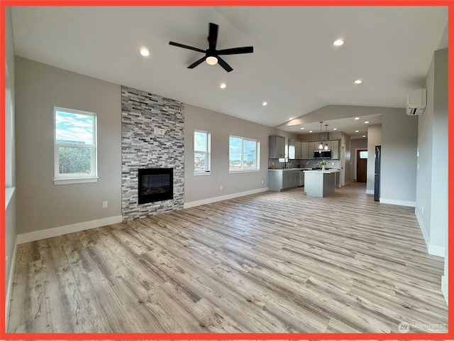 unfurnished living room featuring sink, light hardwood / wood-style flooring, ceiling fan, a stone fireplace, and vaulted ceiling