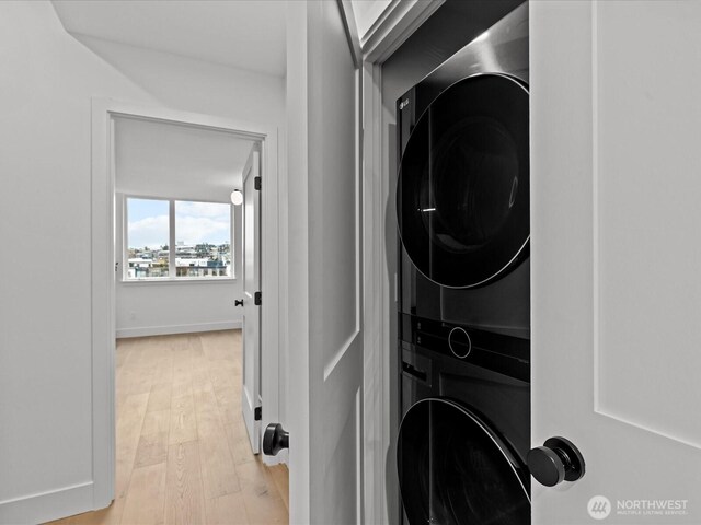 clothes washing area with light wood-type flooring, baseboards, laundry area, and stacked washing maching and dryer